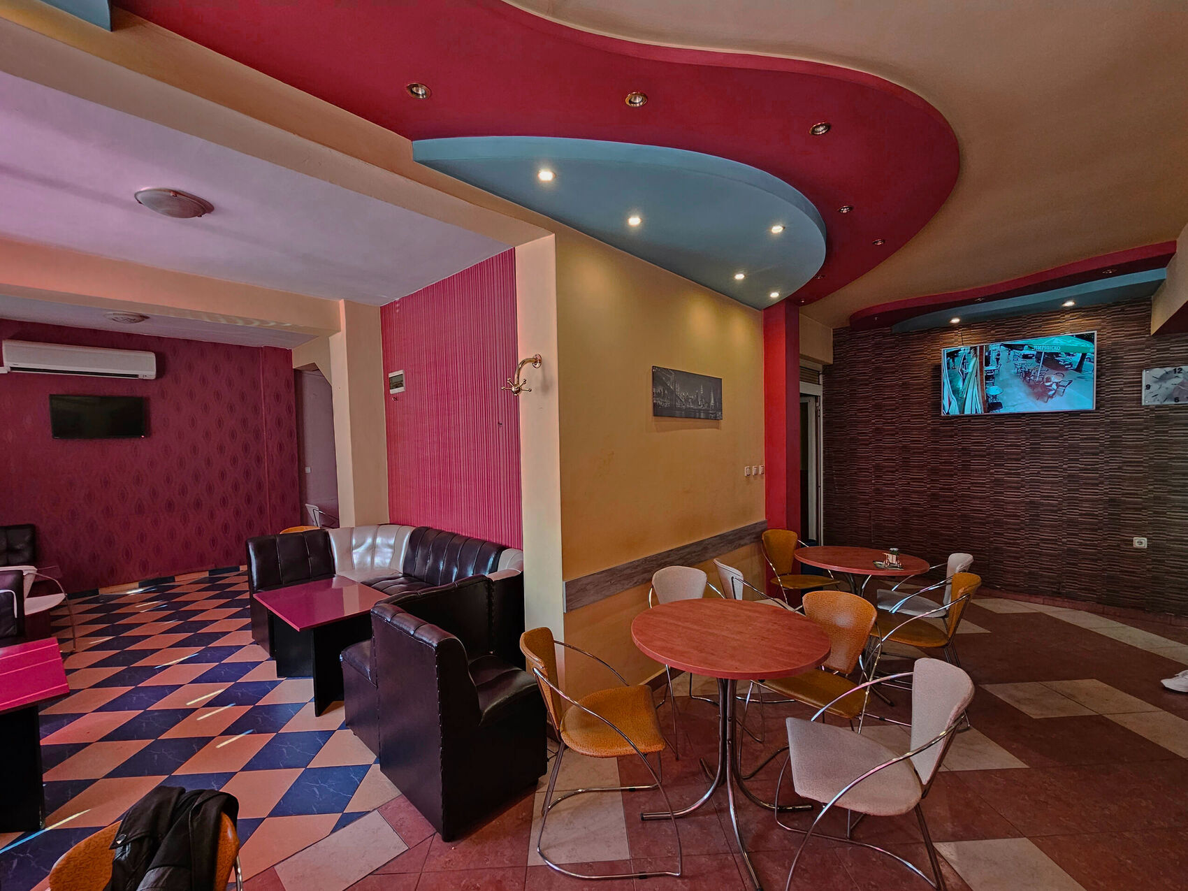 The room before, toward the bar: coloured ceilings and round tables.