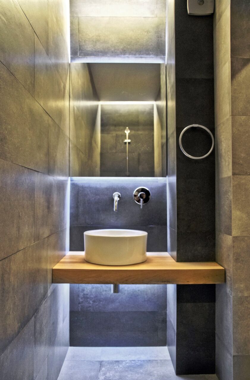 Gäste-WC: ein rundes Becken auf einem Eichenbrett in einem schmalen Steinraum.