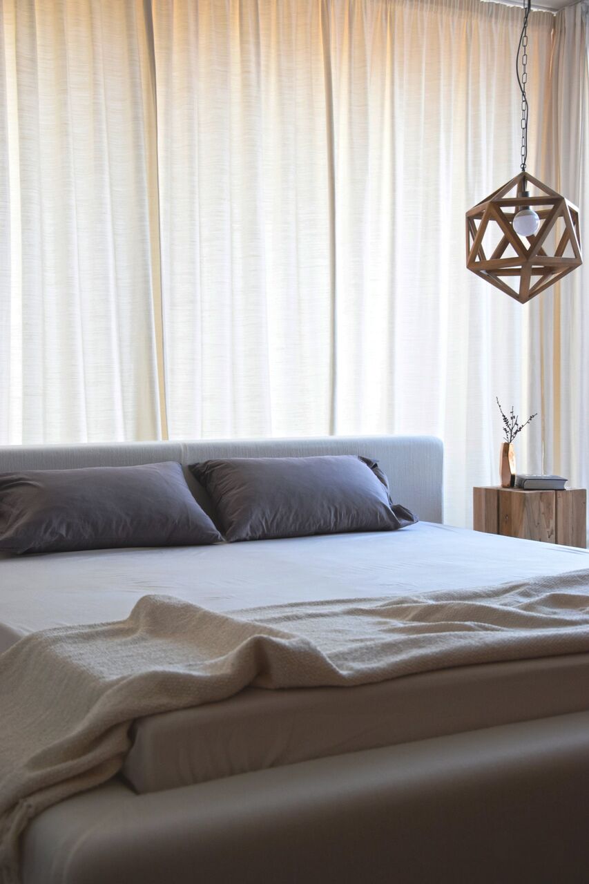 Ein engerer Ausschnitt von Bett und Vorhängen, mit hellen Kissen und Plaid.