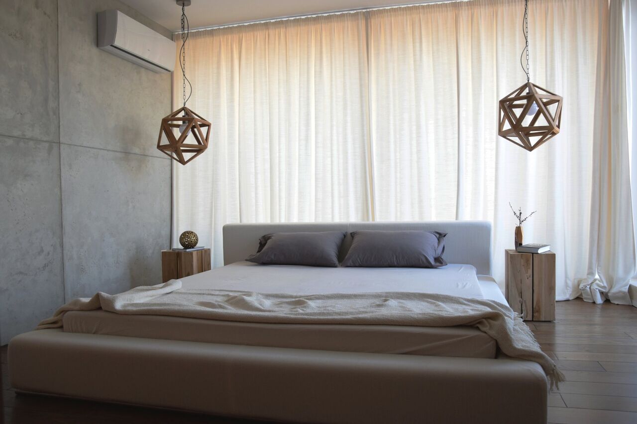Das Schlafzimmer mit zwei geometrischen Lampen und Vorhängen an der Betonwand.
