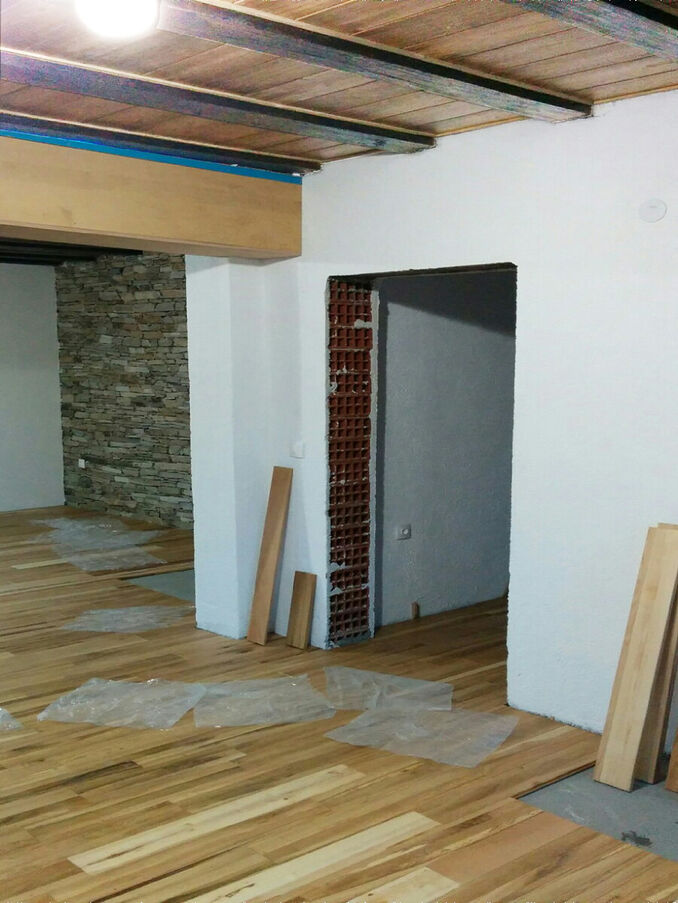 Une photographie de la rénovation : sol de bois, une ouverture vers la pièce suivante et un mur de pierre au fond.