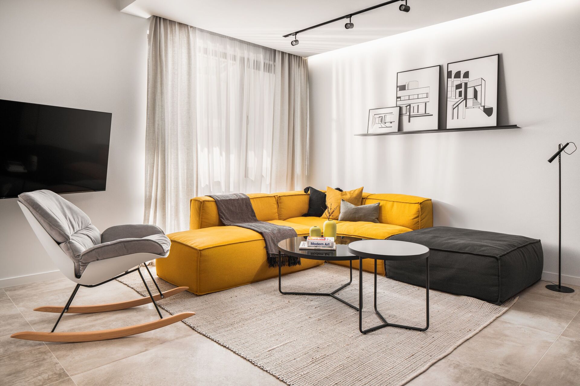 Séjour vers la fenêtre : canapé jaune, rocking beige et téléviseur sur le mur blanc.