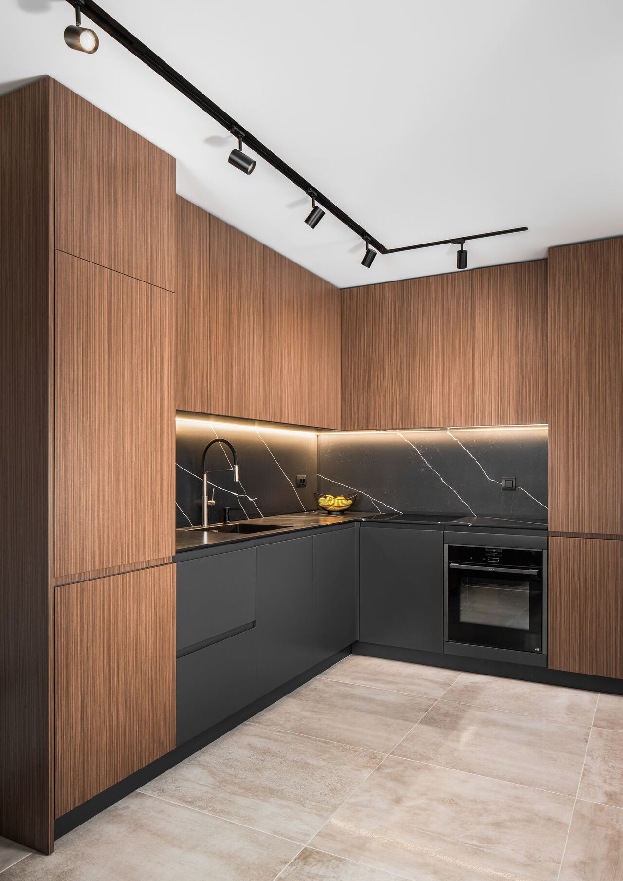 Kitchen corner with walnut cabinets to the ceiling, dark stone and a black track light.