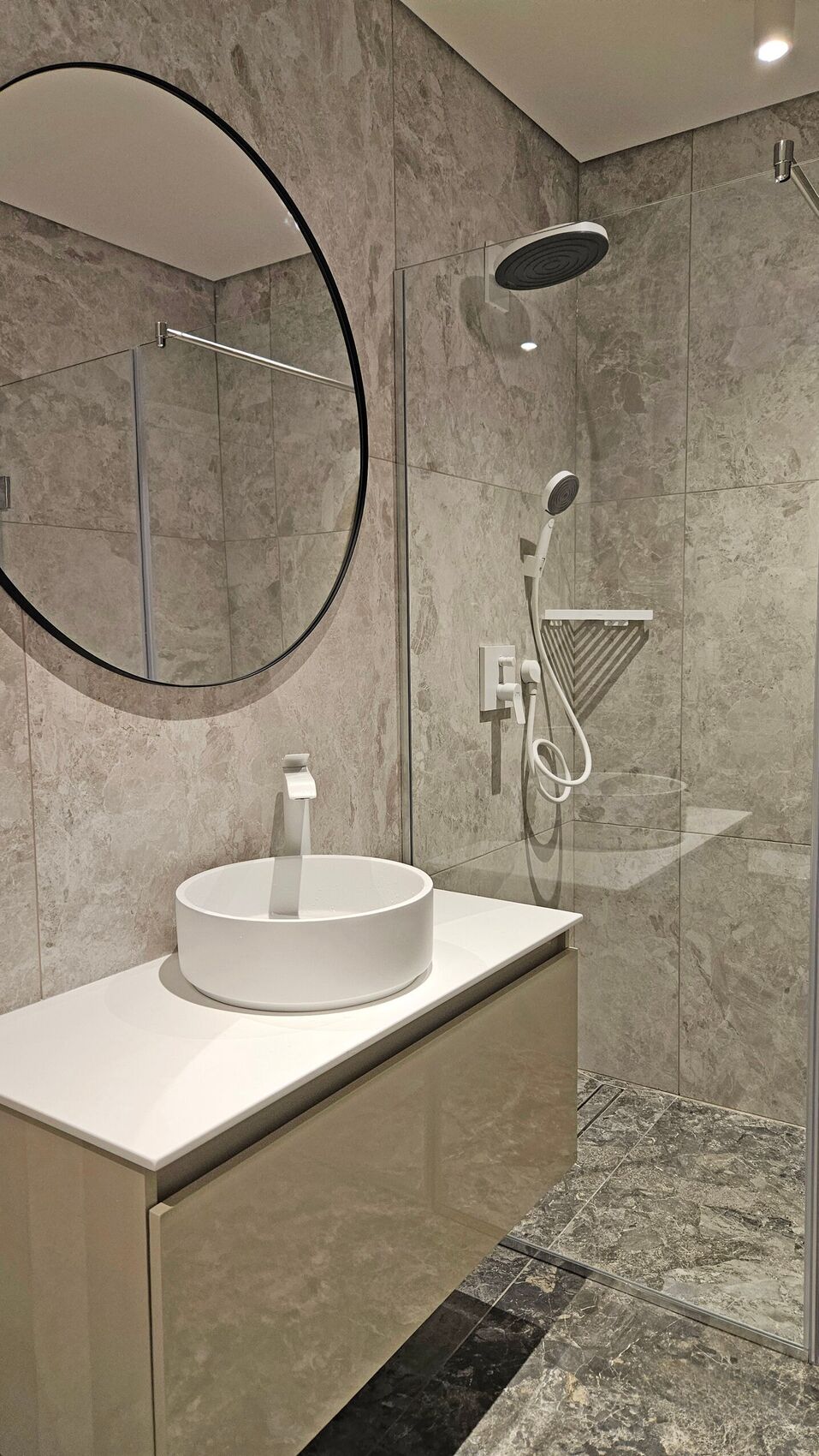 Zweites Bad: Becken, runder Spiegel und Dusche.
