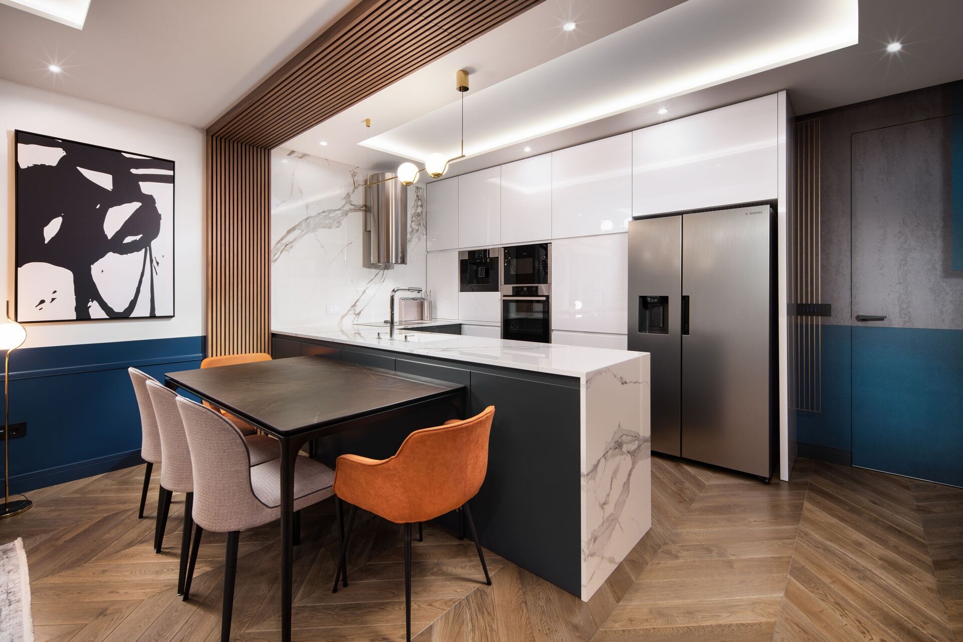 Table à manger contre un îlot de marbre, chaises orange et beige, et réfrigérateur inox.