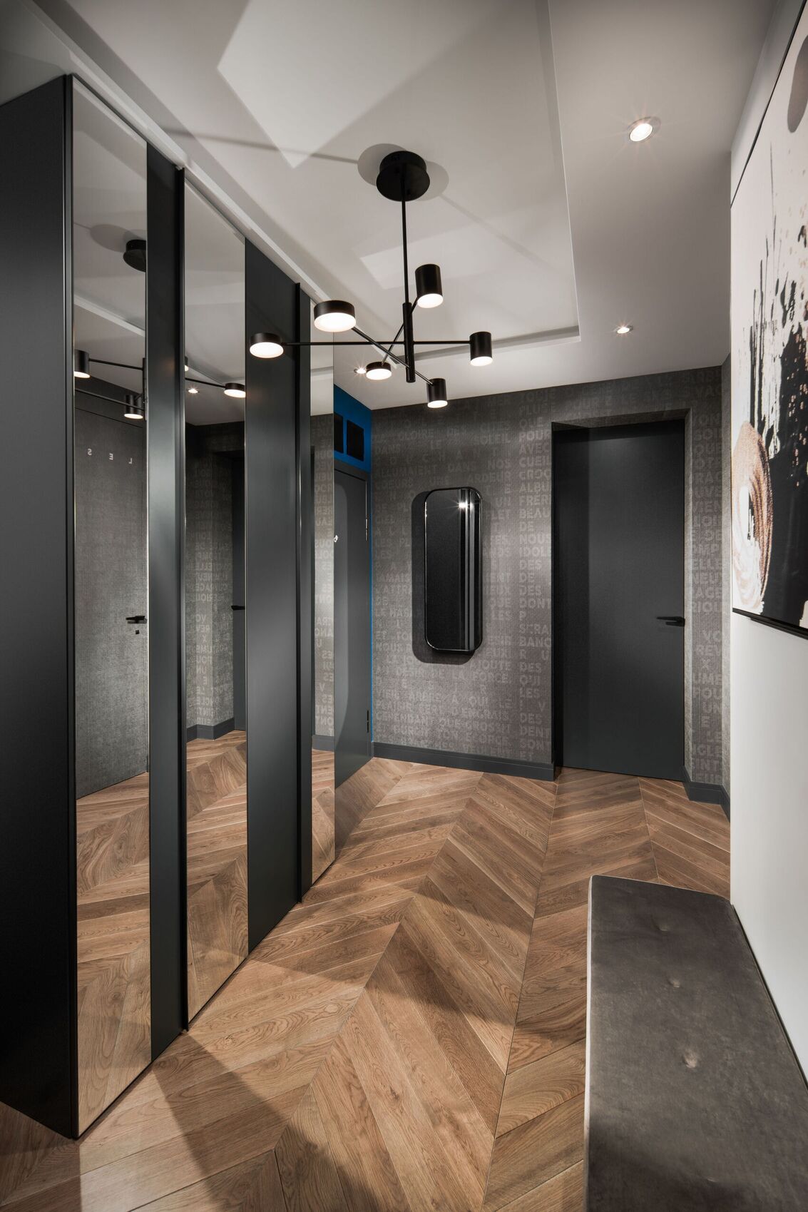 Entrée aux dressings miroir, parquet à chevrons et lustre noir.