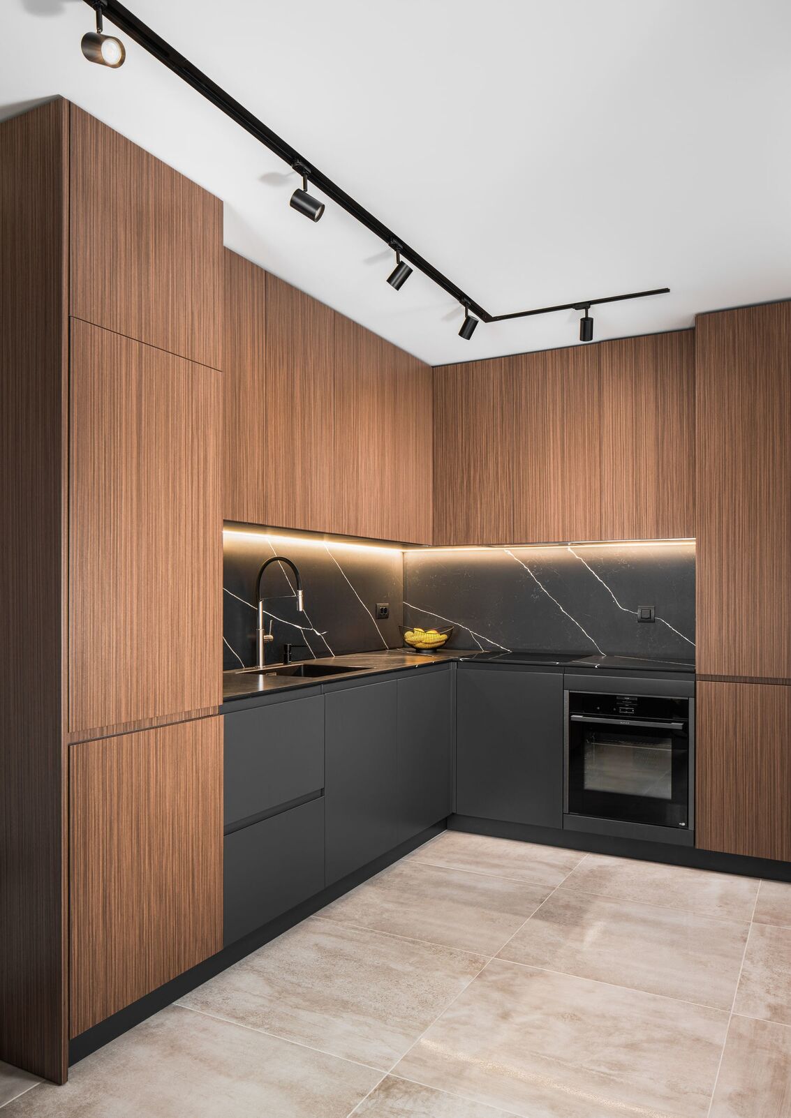 Cocina con armarios de nogal, piedra oscura y riel negro.