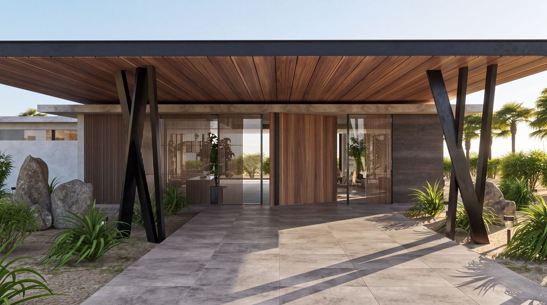 The entrance under the timber soffit, with X-shaped steel supports and boulders in the sand.