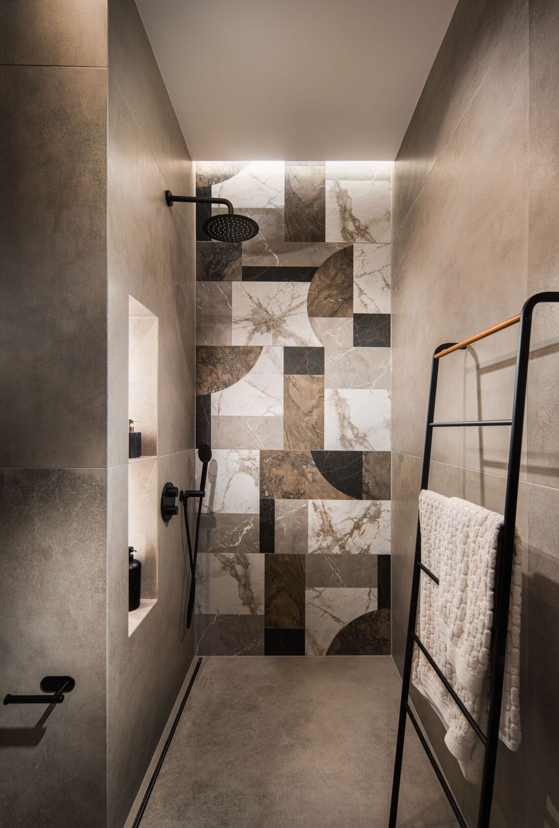 Eine Dusche mit geometrischem Marmorpaneel und schwarzer Armatur.