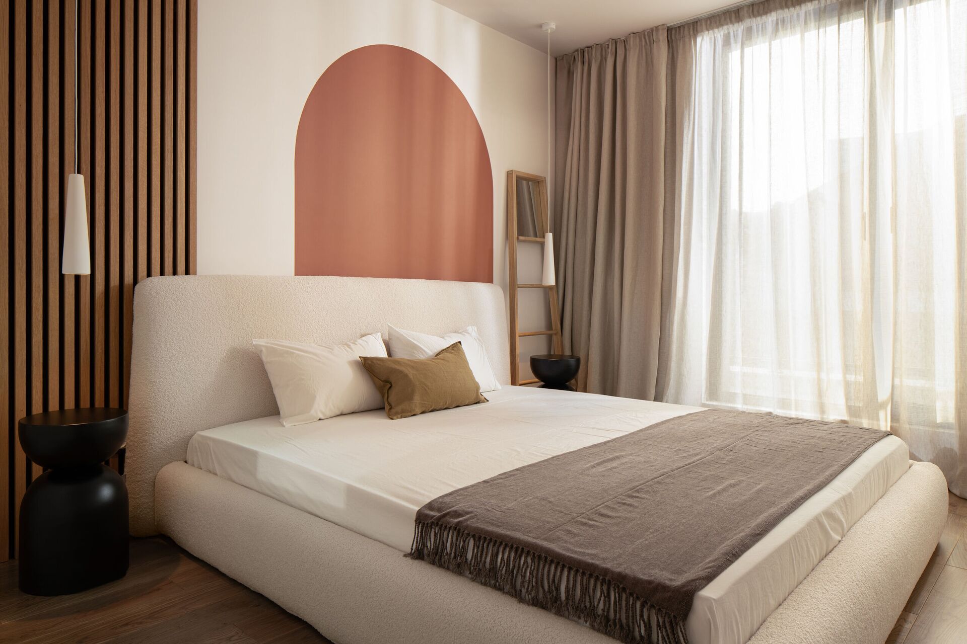 Bedroom with a rounded bed, a terracotta arch and a fluted timber wall.