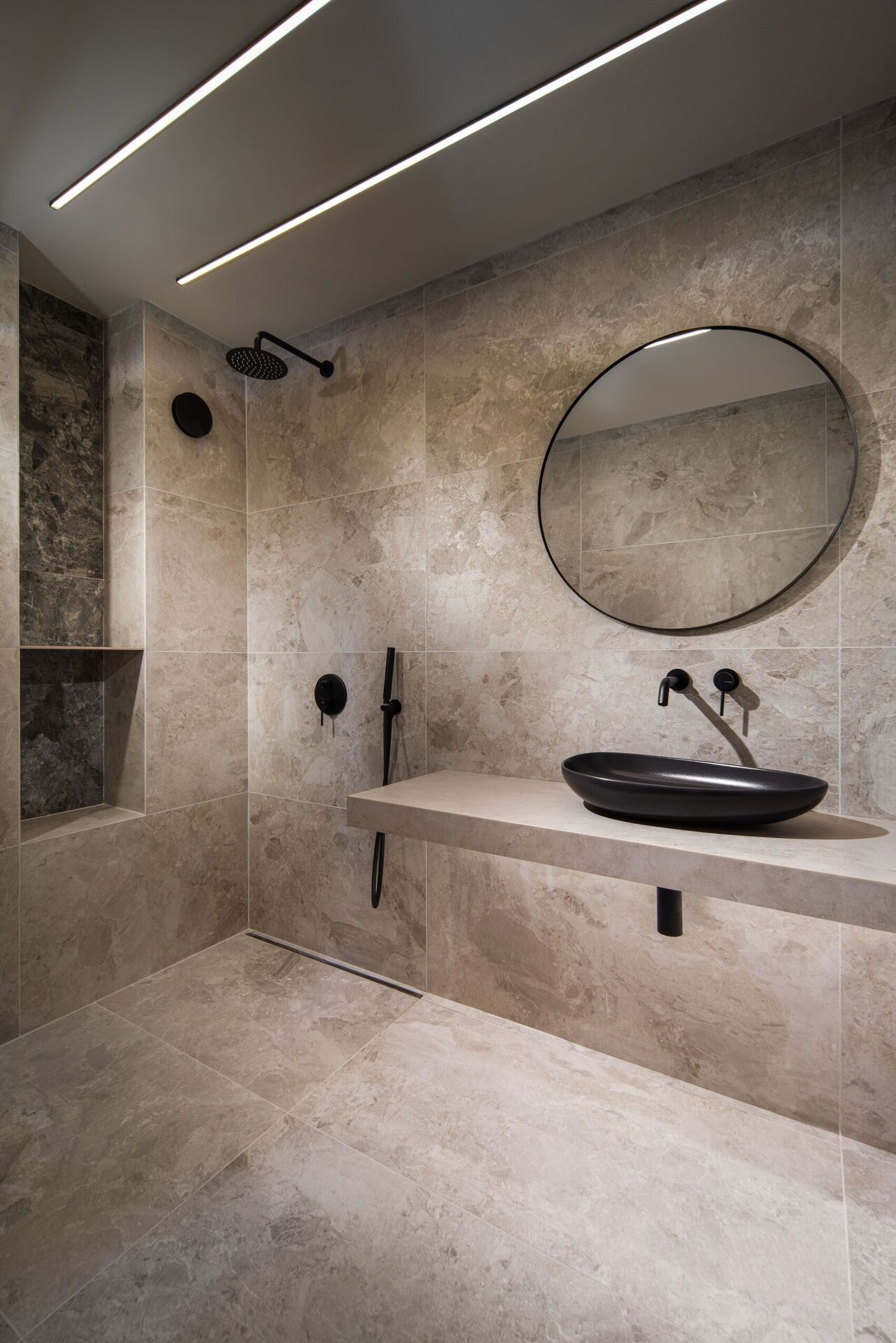 A stone bathroom with a black basin, a round mirror and a walk-in shower.