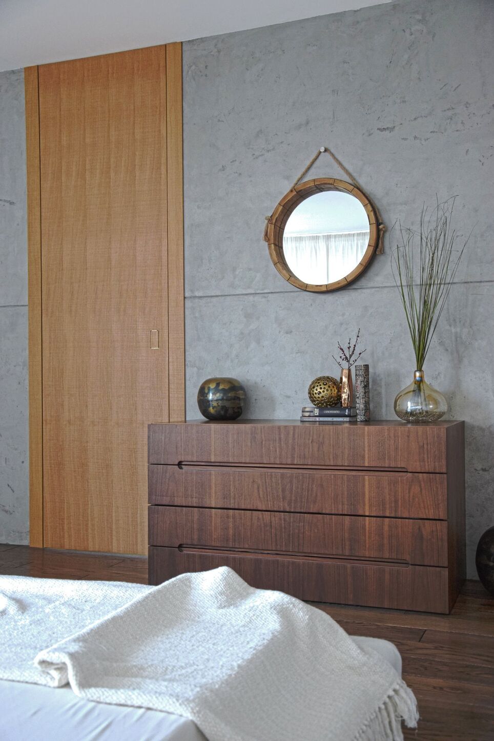 Eine helle Eichentür bis zur Decke mit eingelassenem Griff und eine Holzkommode vor dem Putz.
